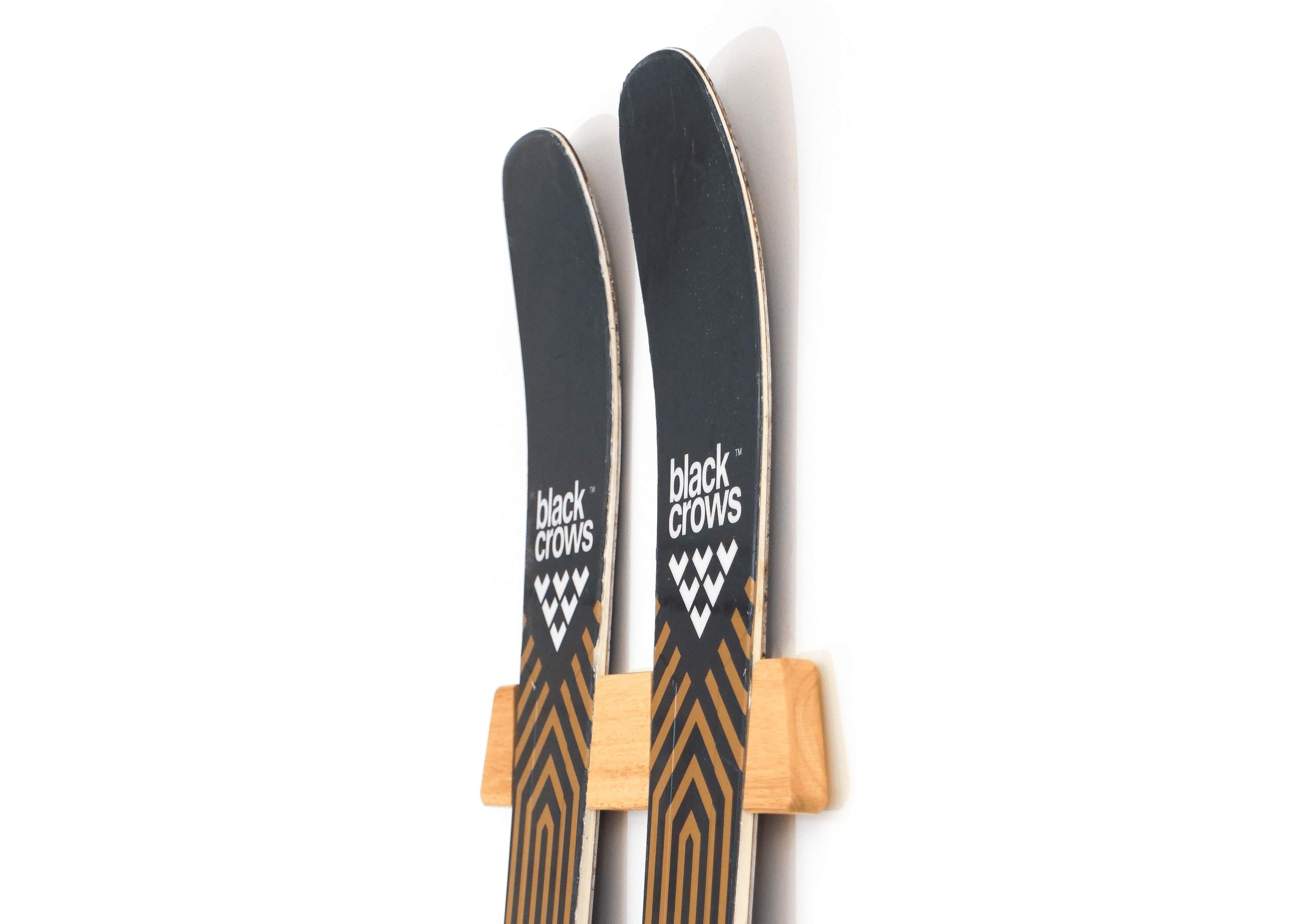 A pair of Black Crows ski tips with black tops and brown wood-grain shafts, resting in a light wood ski rack against a plain white background.