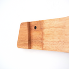 Close-up of a light natural wood object with a visible grain texture and a small pre-drilled hole, photographed against a plain white background.