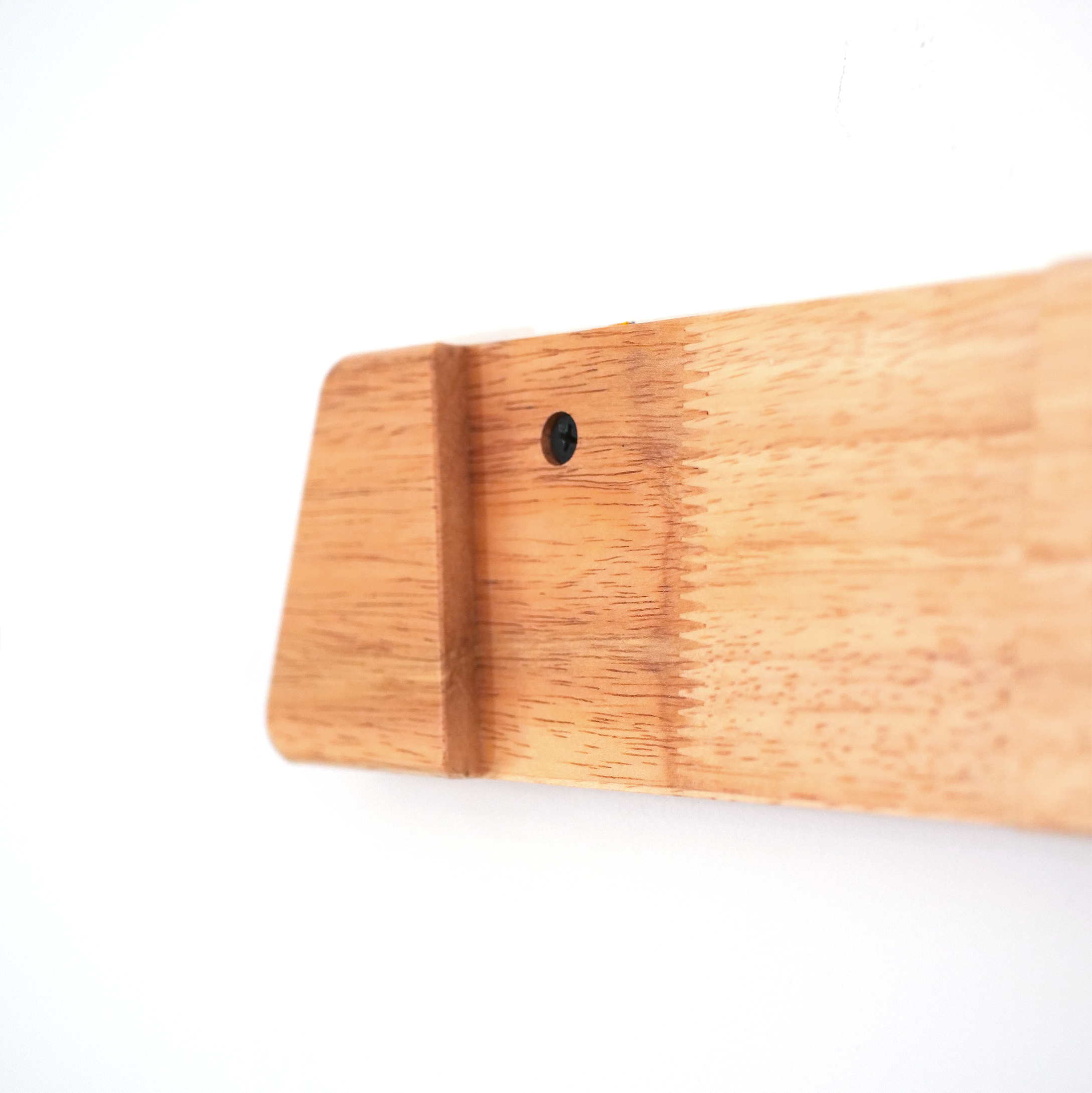 Close-up of a light natural wood object with a visible grain texture and a small pre-drilled hole, photographed against a plain white background.